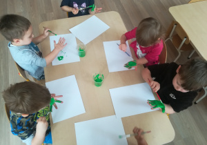 Dzieci odbijają dłoń w farbie na kartce papieru